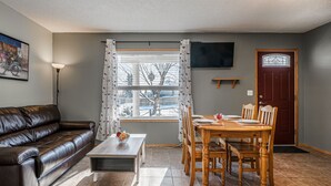 A living room with a brown leather sofa, a wooden coffee table, and a dining area with a wooden table and chairs. - Entire large house! 8 bedrooms & 4Baths! Close to airport! (Calgary)
