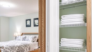A bedroom with a wooden bed, a nightstand, and a wall-mounted shelf with folded towels. - Entire large house! 8 bedrooms & 4Baths! Close to airport! (Calgary)