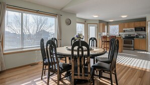 A dining area with a round table and chairs, a kitchen with wooden cabinets, and a clock on the wall. - Entire large house! 8 bedrooms & 4Baths! Close to airport! (Calgary)