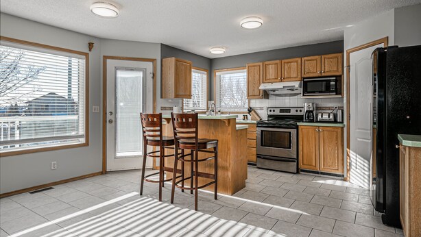 A modern kitchen with wooden cabinets, a central island, and built-in appliances. - Entire large house! 8 bedrooms & 4Baths! Close to airport! (Calgary)