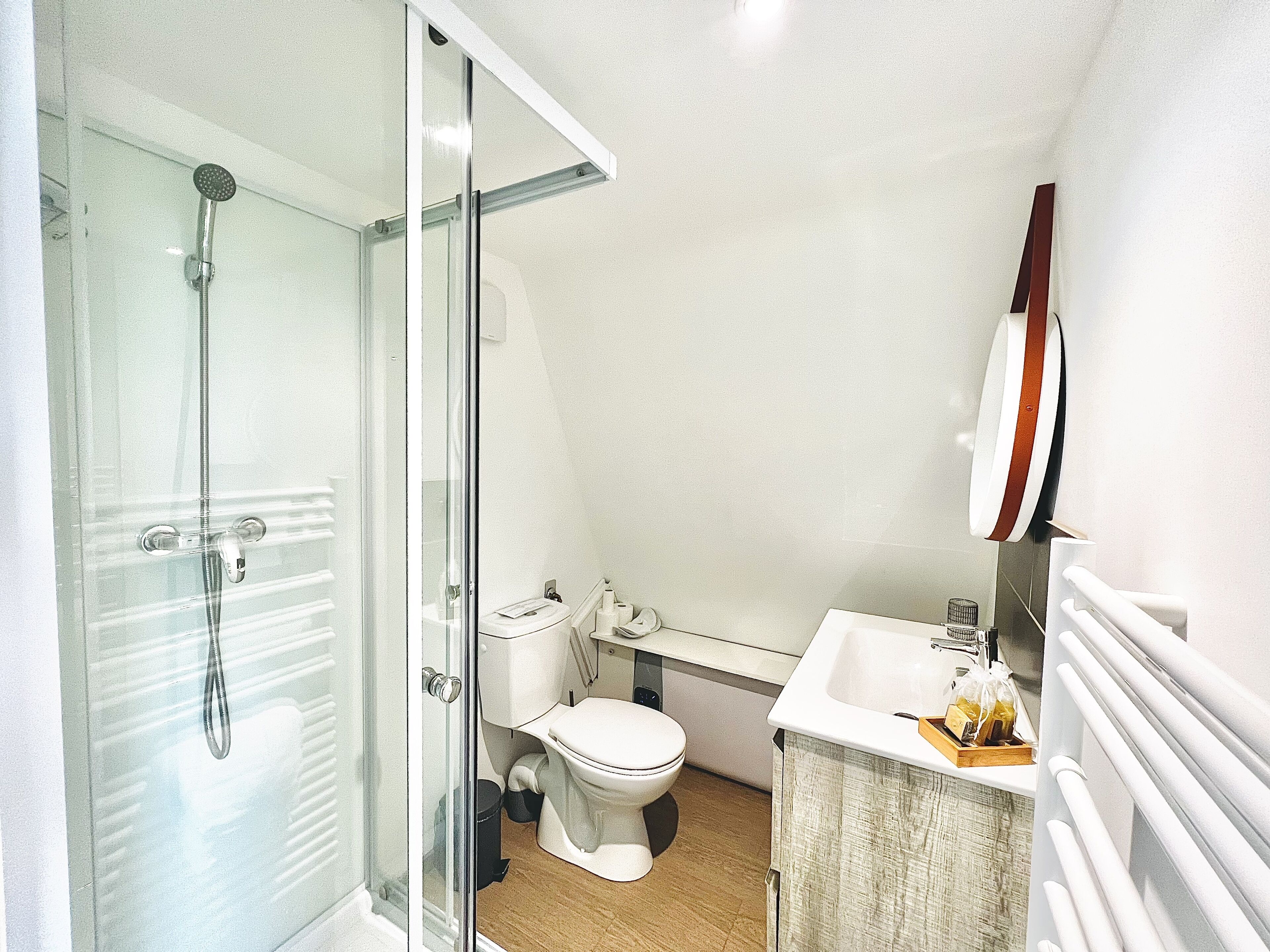 Een badkamer met een douchecabine van glas, een toilet en een wastafel met een handdoekhouder.