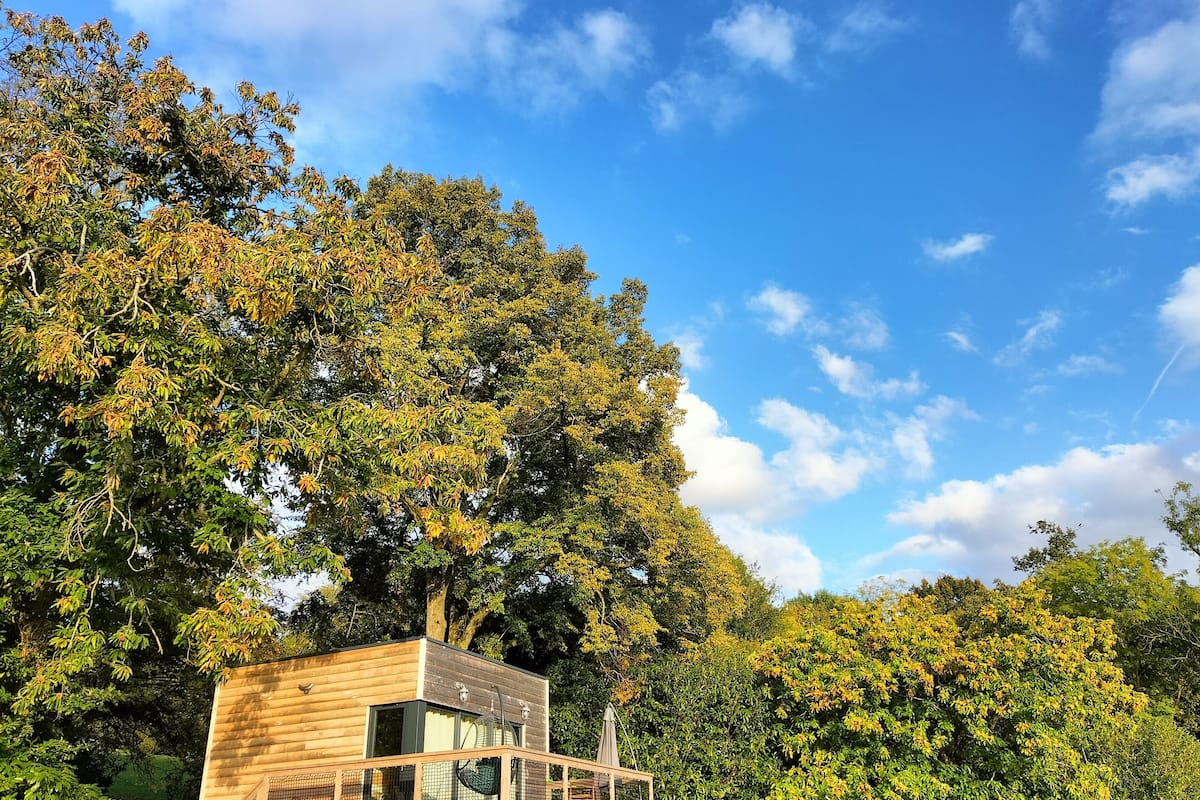 Une cabane en bois dotée d’un balcon, entourée d’une forêt dense et surplombant un ciel dégagé.