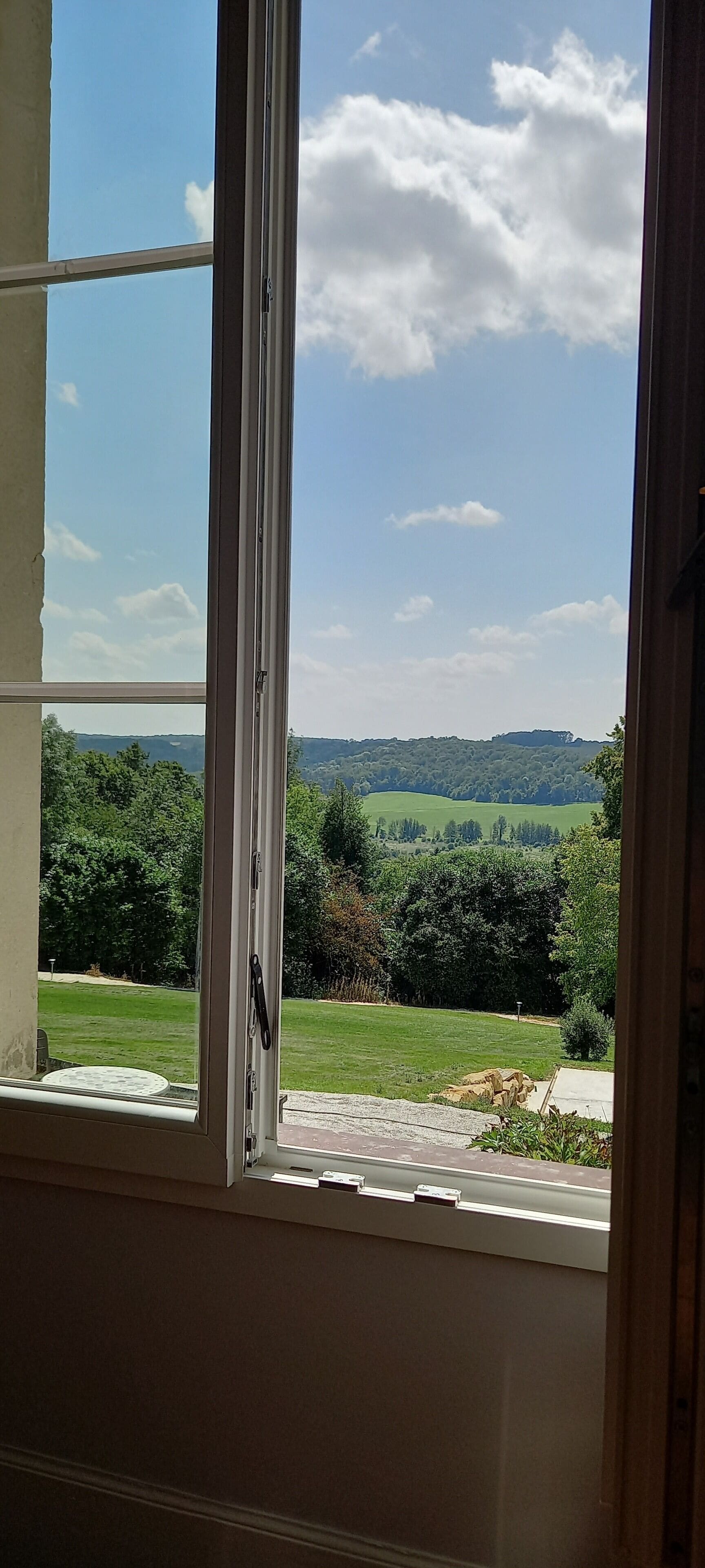 A room with a large window offering a view of a green landscape with trees and hills.