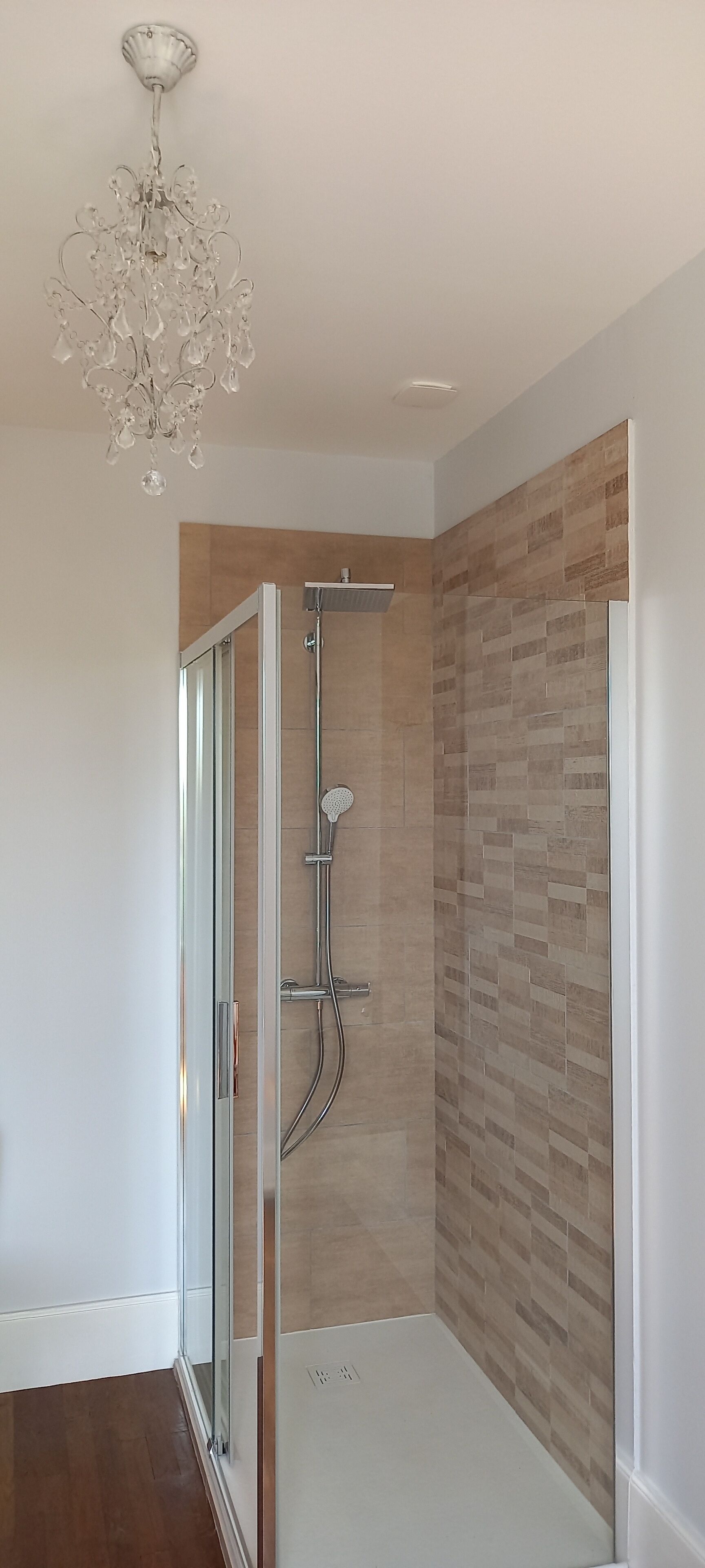 A modern bathroom with a glass shower enclosure, a showerhead, and a chandelier.