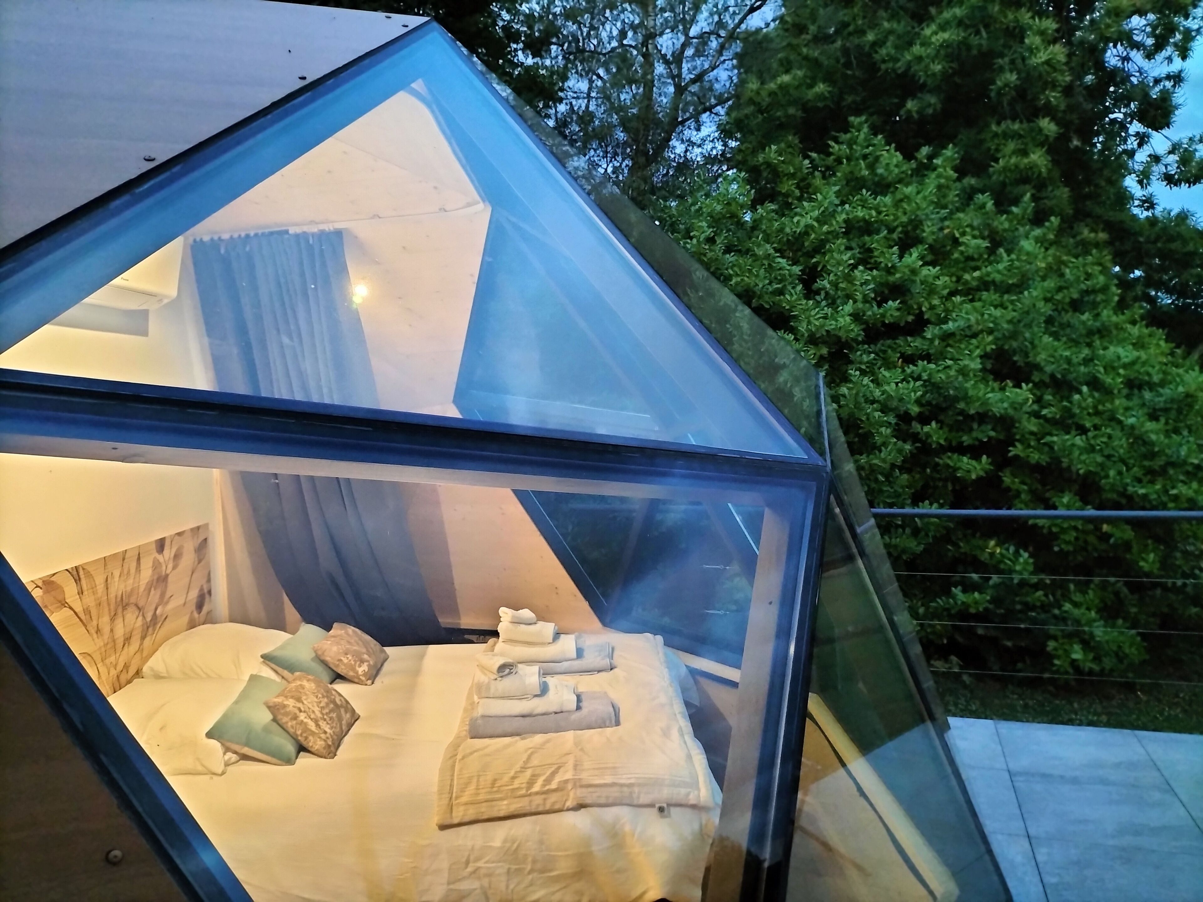 Een moderne slaapkamer met glazen wanden, een bed, kussens en netjes opgevouwen handdoeken.