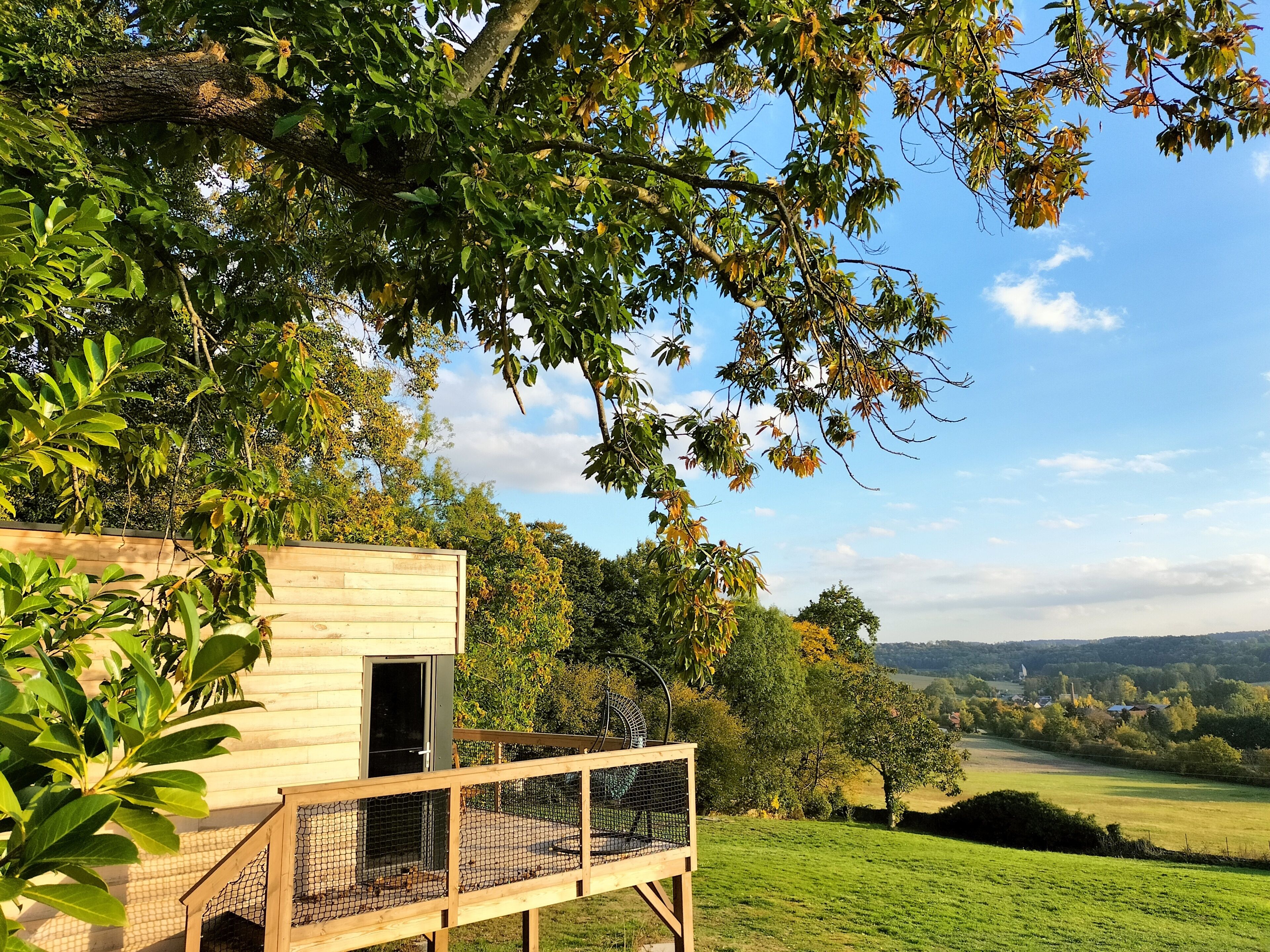 A wooden cabin with a fenced deck, surrounded by trees and a view of a rural landscape.