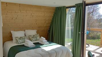 Quarto com cabeceira de madeira, cortina verde e vista para o exterior.