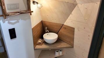 A bathroom with a white sink, wooden accents, a towel rack, and a wall-mounted light fixture.