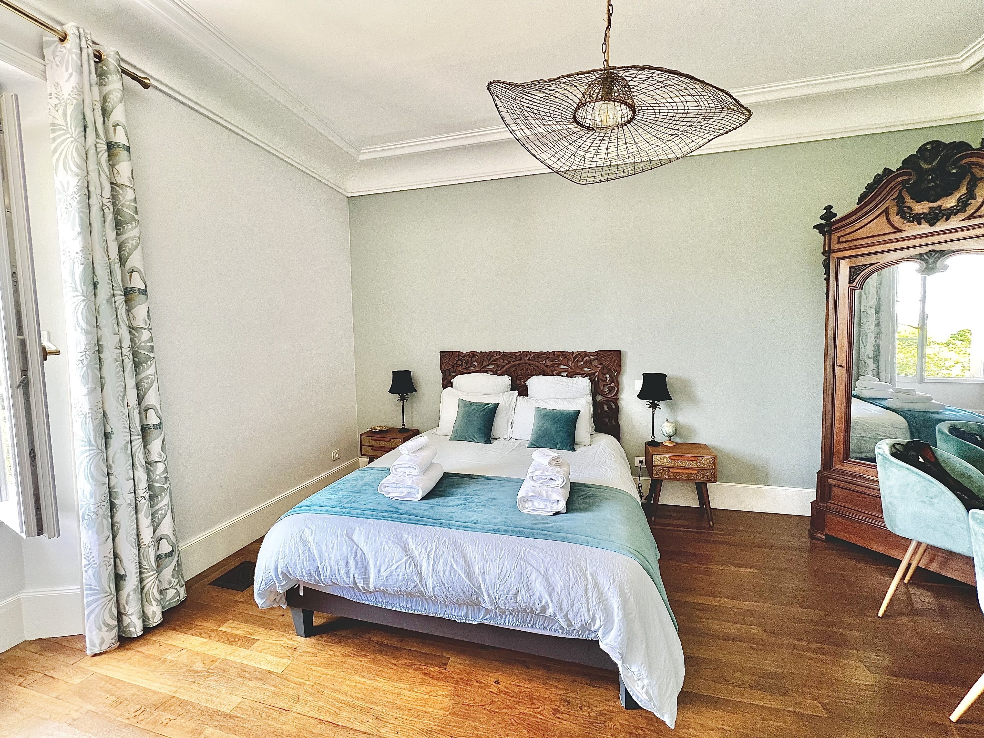A neatly arranged bedroom with a bed, bedside tables, a mirror, and a hanging light fixture.
