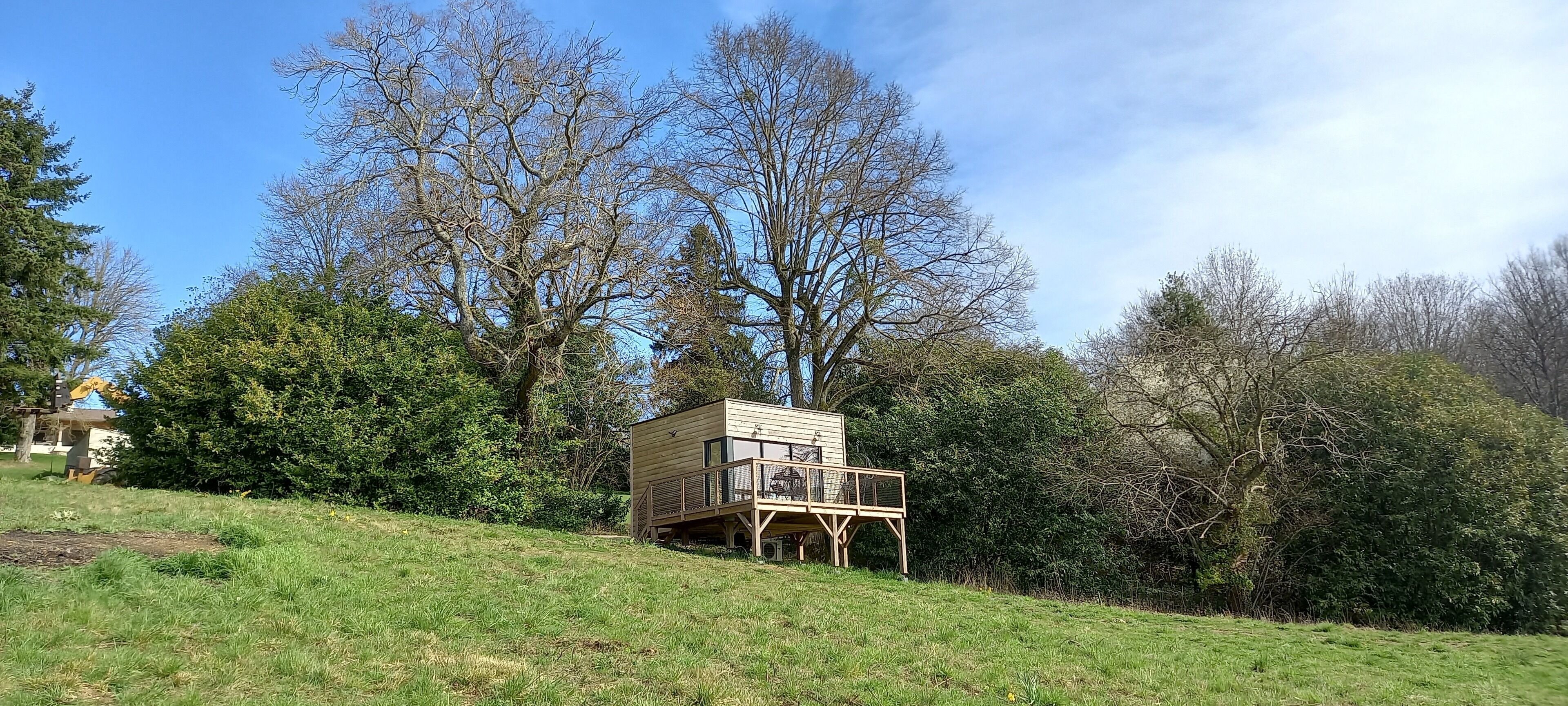 A wooden cabin with a deck, surrounded by trees and greenery.