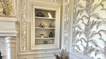 A room with a decorative fireplace, a white mantelpiece, and a wall with a tropical leaf pattern.