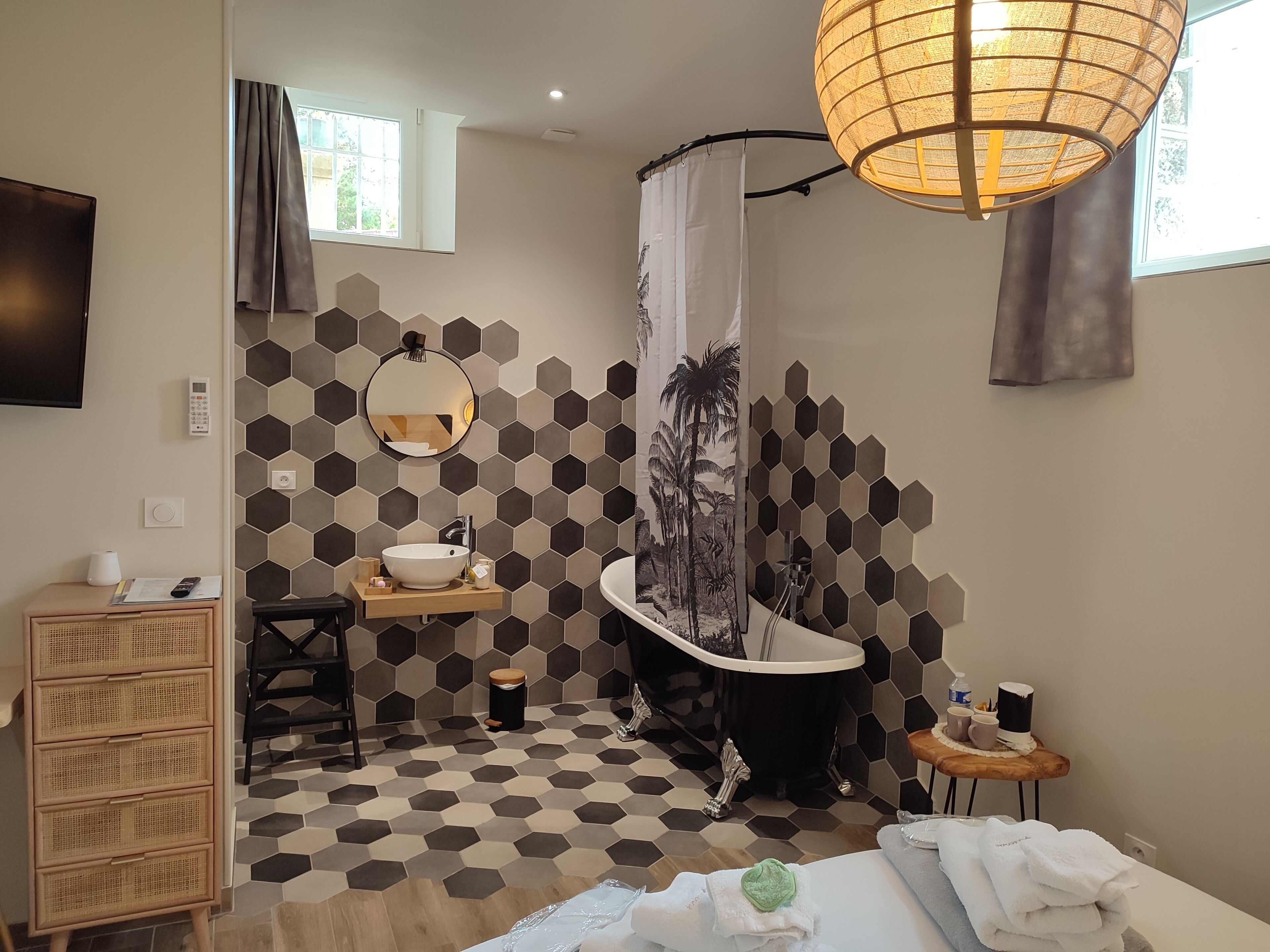 A modern bathroom with a hexagonal tile floor, a freestanding bathtub, a round mirror, and a wooden vanity.