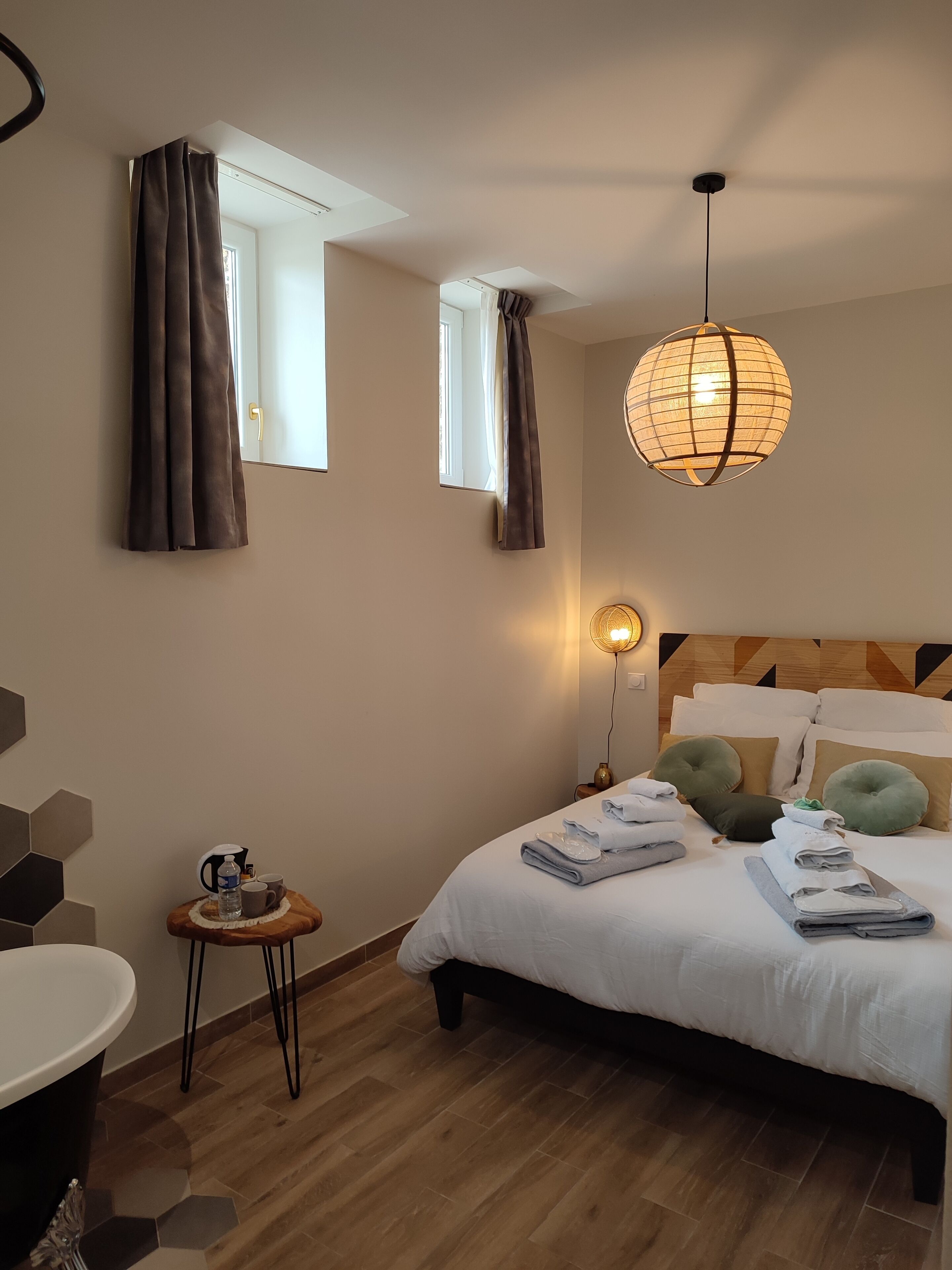 Une chambre d’hôtel avec un lit, une petite table avec une bouilloire et des tasses, une chaise et une fenêtre avec des rideaux.