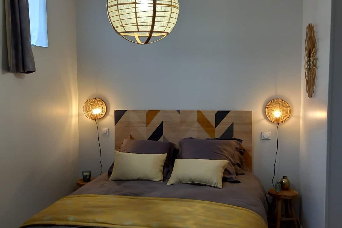 Une chambre à coucher avec un lit, des lampes de chevet, un luminaire fixé au mur et une porte.