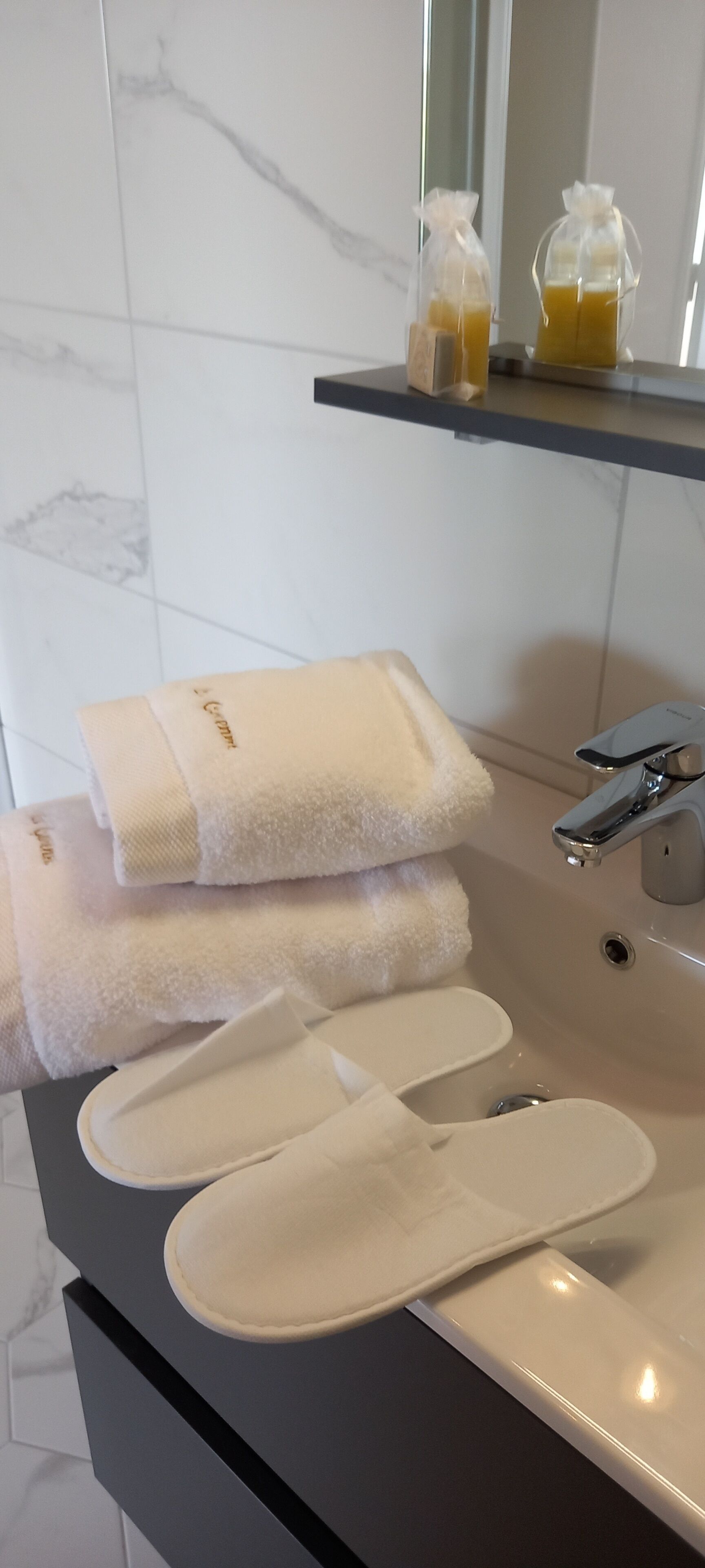 Et badeværelse med håndvask, to håndklæder og et par badesandaler.