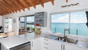 A modern kitchen with a large window overlooking a scenic view, wooden ceiling beams, and a marble countertop. - Nelson's Lookout - Russell Holiday Home (Russell)
