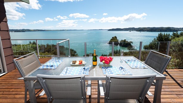 A dining table with chairs on a deck overlooking a body of water. - Nelson's Lookout - Russell Holiday Home (Russell)