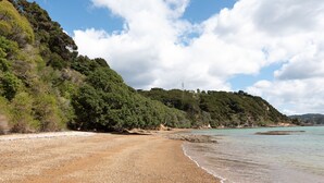 A beach with pebbly shore, dense greenery, and a clear sky. - Nelson's Lookout - Russell Holiday Home (Russell)