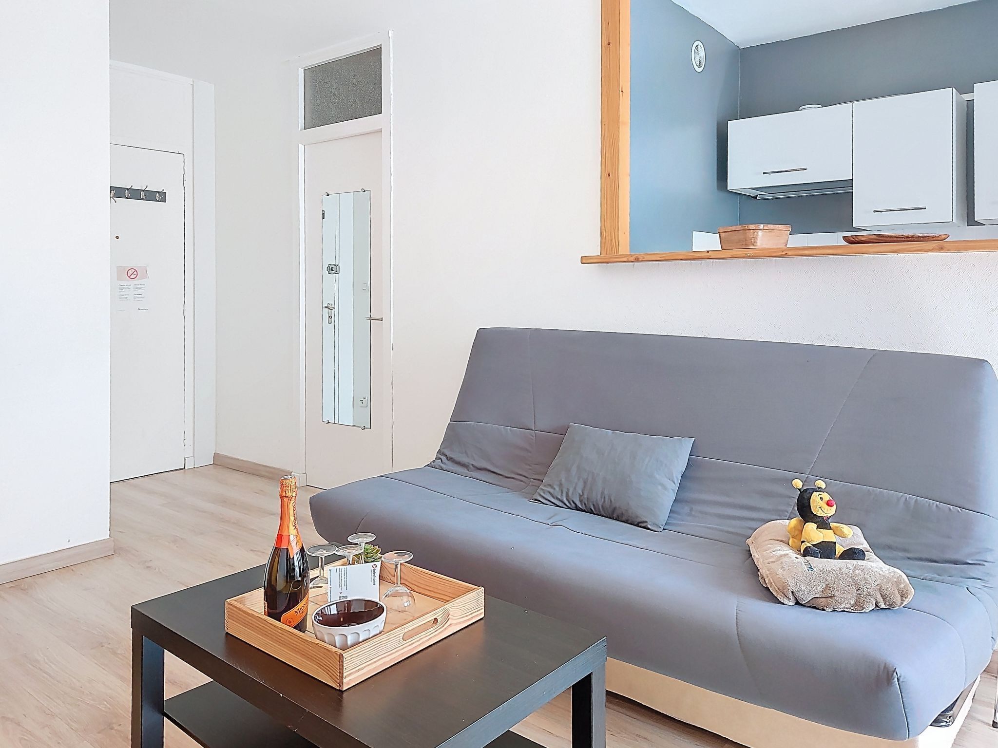 En moderne stue med en grå sofa, et træsofabord med en flaske og glas, og en lille blød legetøj på sofaen.
