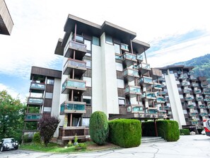 Um edifício residencial com vários andares, varandas, área de estacionamento e montanhas ao fundo.