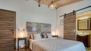 Quarto com uma cama grande, paredes de madeira, cabeceira com padrão geométrico, mesa de cabeceira com luminária e teto de madeira.
