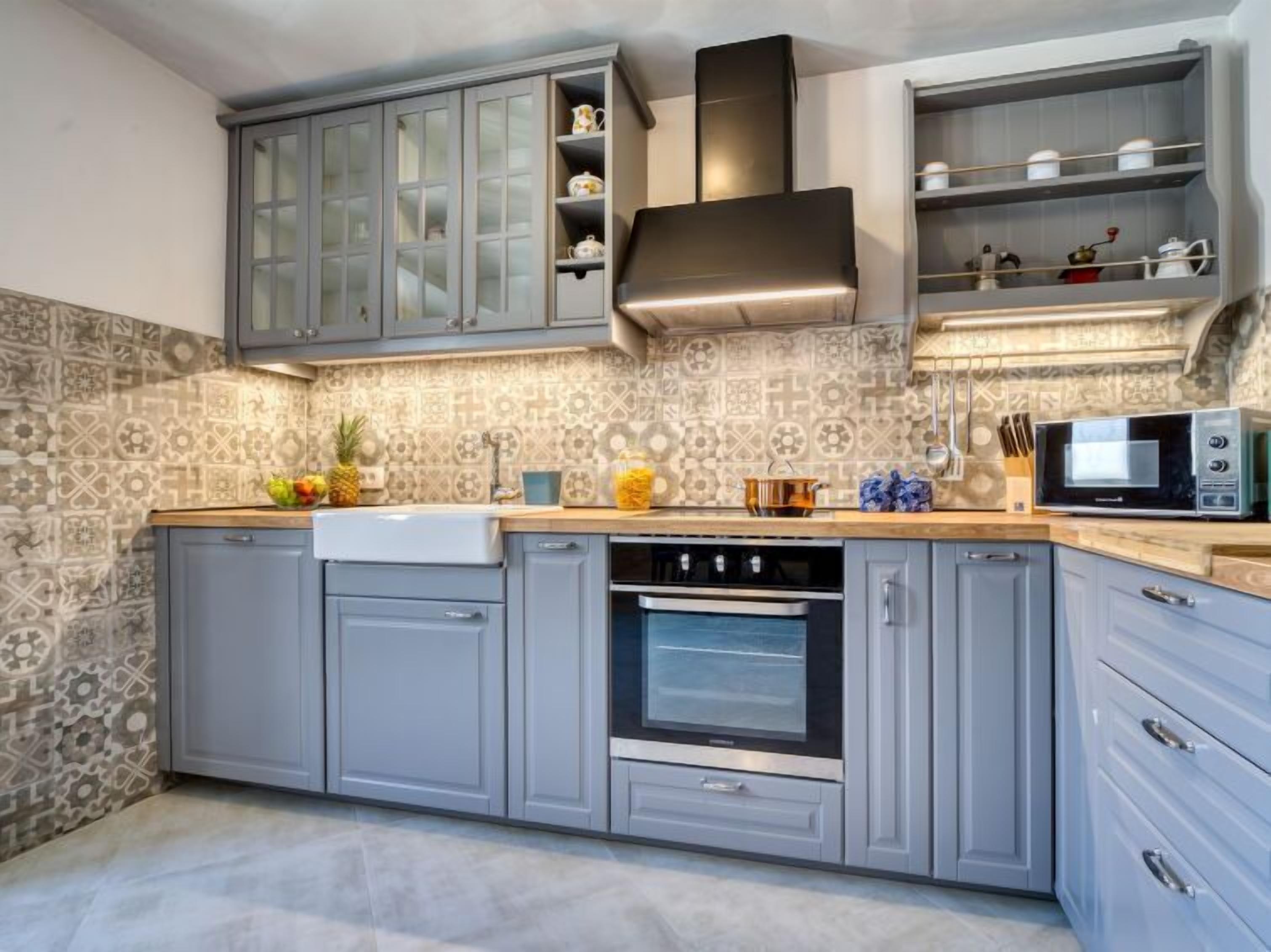 A modern kitchen with grey cabinets, a built-in oven, a microwave, and a patterned backsplash.