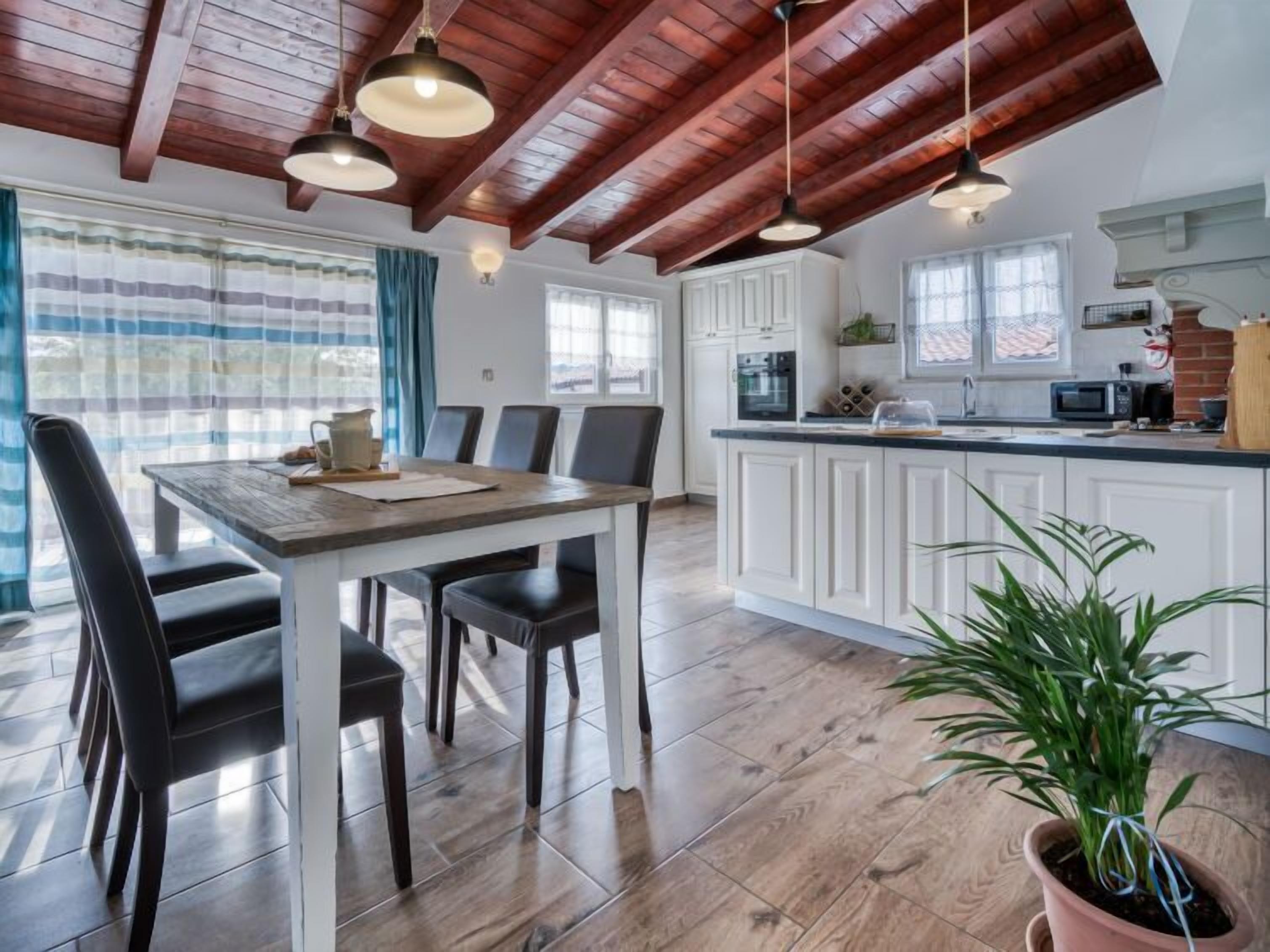 A modern kitchen with white cabinets, a wooden dining table, and black chairs. There is a potted plant on the counter.