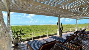 A covered outdoor seating area with wooden loungers and a view of a green landscape.