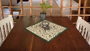 A wooden table with a green patterned placemat, a potted plant, and a small decorative item.