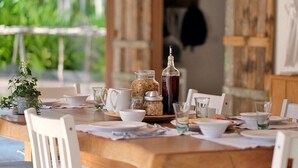 A wooden dining table set with white chairs, a potted plant, and various dishes and drinks.