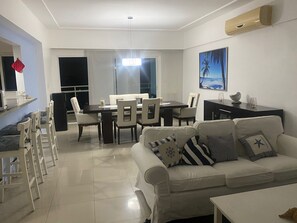 Uma sala de estar moderna com sofá, mesa de jantar, cadeiras e uma área de cozinha com geladeira e fogão.