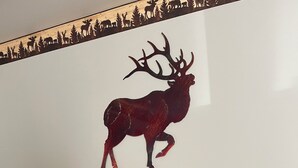 Um console de madeira com silhueta decorativa de veado, um vaso de girassóis e um pequeno enfeite de pinho.