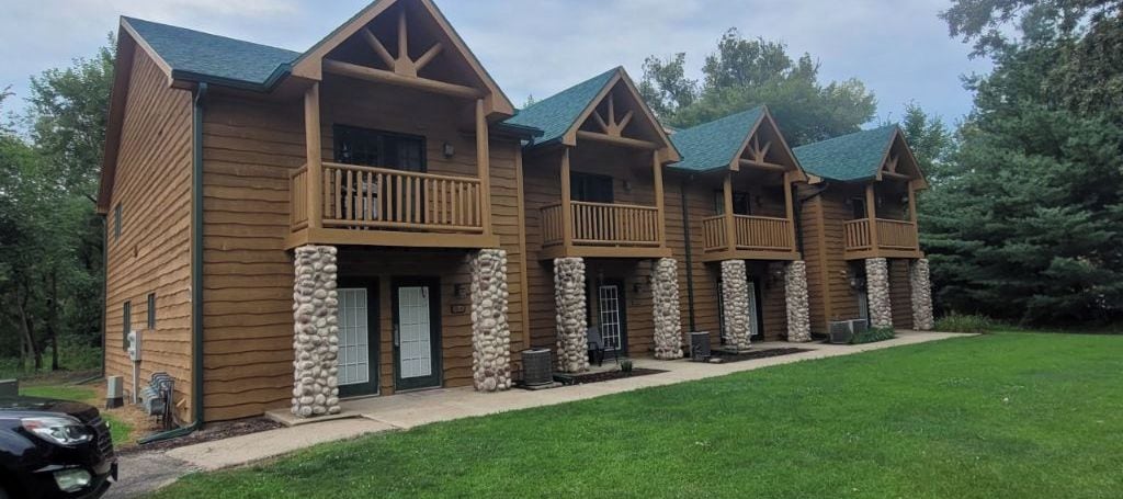 Une rangée de cabanes en bois, dotées de piliers en pierre, de balcons et d’une pelouse verdoyante.