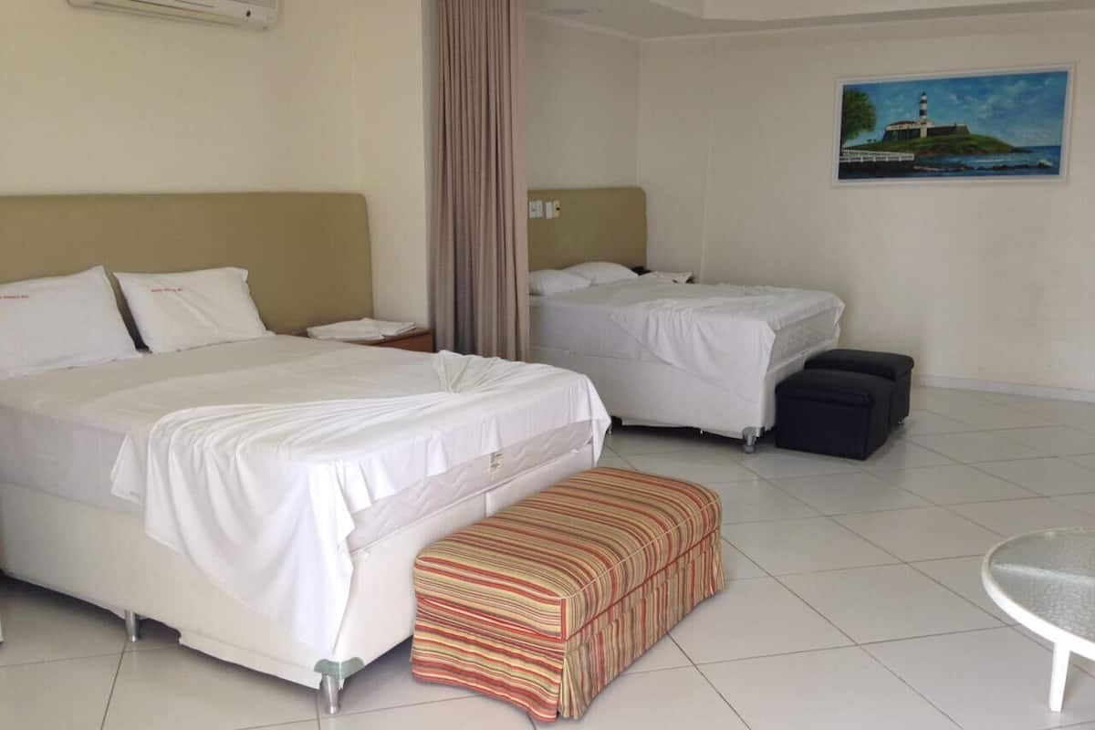 A hotel room with two beds, a small table, a bench, and a painting on the wall.