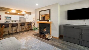Una sala de estar moderna con chimenea, una zona de cocina y una barra con taburetes.