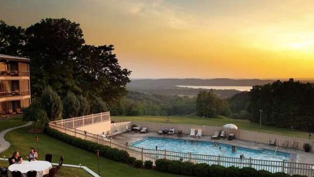 Un área de piscina con vistas al paisaje, un edificio con balcón y una zona de comedor con mesas y sillas.