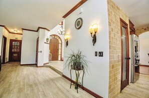 A hallway with a wooden floor, a potted plant, wall sconces, a clock, and an exit sign.