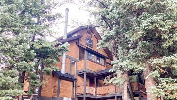 Eine mehrstöckige Holzhütte mit Schornstein, umgeben von Bäumen.