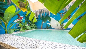 Ein Pool mit gefliesten Rändern, umgeben von tropischer Bepflanzung und einem Wandgemälde von Palmen und einem Vogel.
