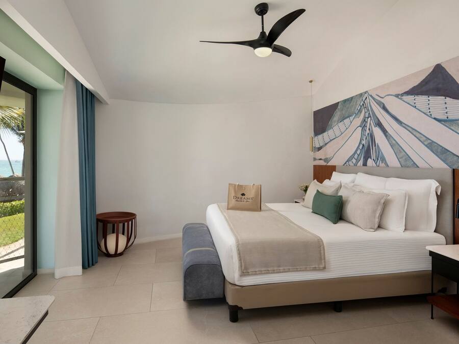 A bedroom with a bed, a ceiling fan, a painting, a small table, and a bench.