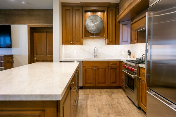 A kitchen with wooden cabinets, a marble countertop, a stainless steel refrigerator, and a built-in oven.