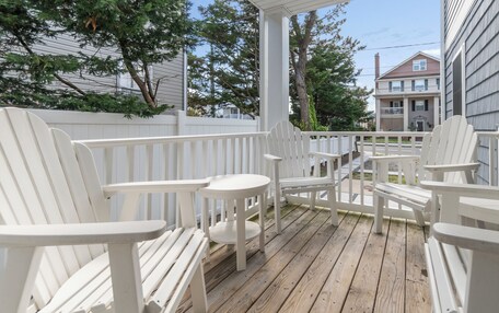 A wooden deck with white Adirondack chairs and a small round table.