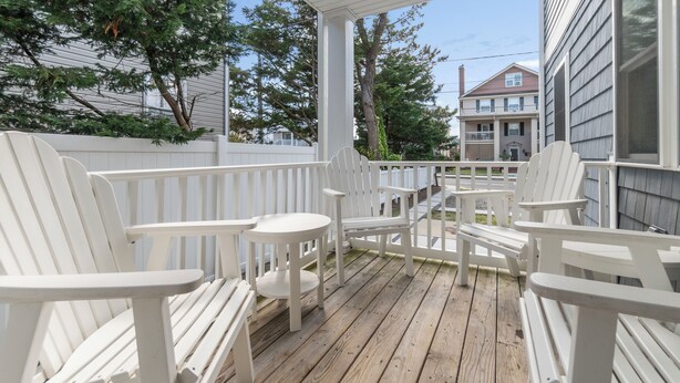 A wooden deck with white Adirondack chairs and a small round table. - Safari Apartments (Ocean City)