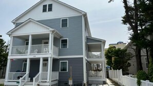 A two-story house with a front porch, a balcony on the second floor, and a small front yard. - Safari Apartments (Ocean City)