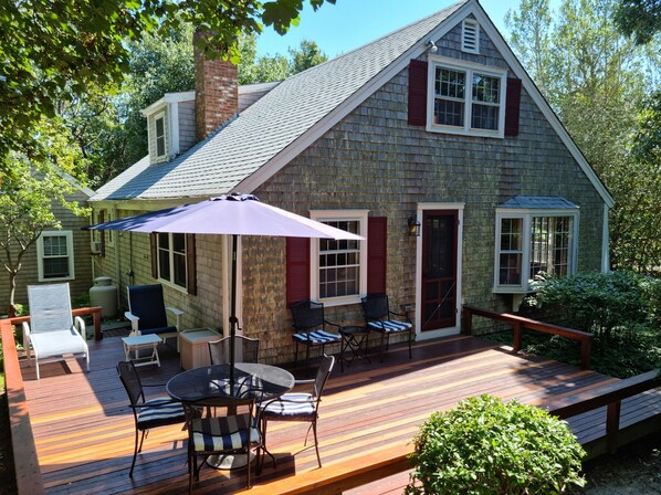 A wooden deck with a table and chairs, a covered patio area, and a stone house with a chimney.