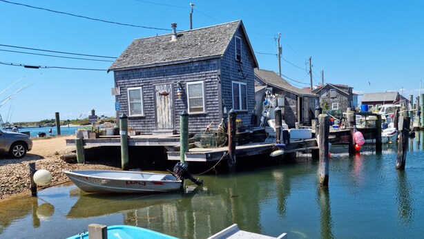 Un barco amarrado, una casa de madera y un cielo azul despejado.