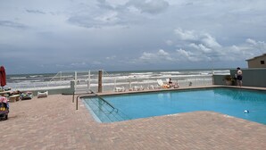 Un área de piscina con vista al océano, una terraza amurallada y sillas de descanso.
