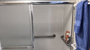 Un área de ducha con puerta de vidrio, un perchero con una toalla azul y un estante con artículos de aseo.