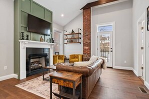 A living room with a fireplace, a sofa, a coffee table, and a TV mounted on a green wall. - Luxurious Design | Easy Access to Downtown Pittsburgh | Sleeps 4 (Pittsburgh)