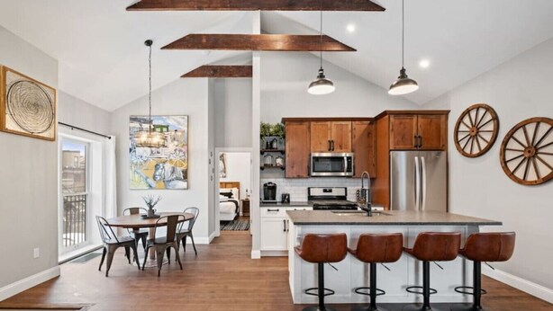 Une cuisine moderne avec des meubles en bois, un îlot central doté de tabourets, un éclairage suspendu et un coin repas avec une table et des chaises.